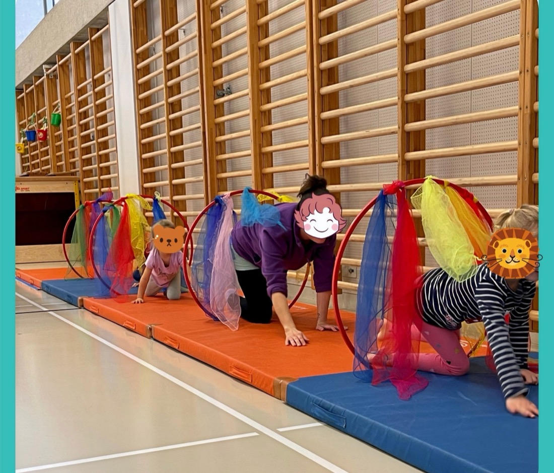 Kinder und Mamis kriechen durch bunte Reifen in der Turnhalle